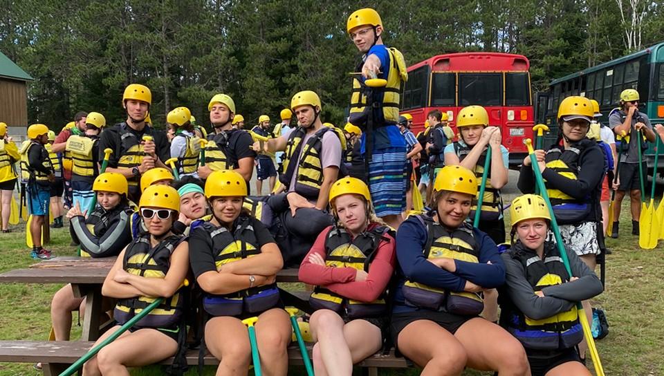 A group of U N E students wearing helmets, life vests, and holding paddles